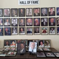 Hall of Fame display featuring framed portraits of inductees arranged on a wall, with additional photos on a table below, celebrating their achievements.