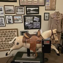 Vintage rocking horse with saddle on a stand, surrounded by historical photographs and memorabilia, showcasing a nostalgic theme.