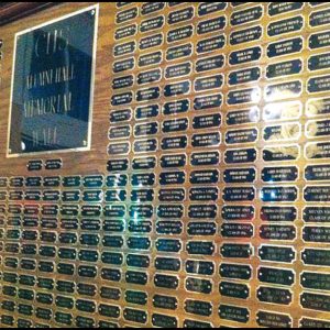 Plaque wall at a memorial theater displaying numerous engraved name plates honoring contributors and alumni, highlighting their legacy and support.