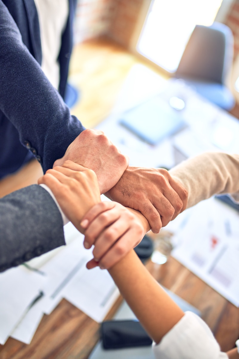 Hands of diverse individuals clasped together over a wooden table, symbolizing teamwork and collaboration in a business setting.